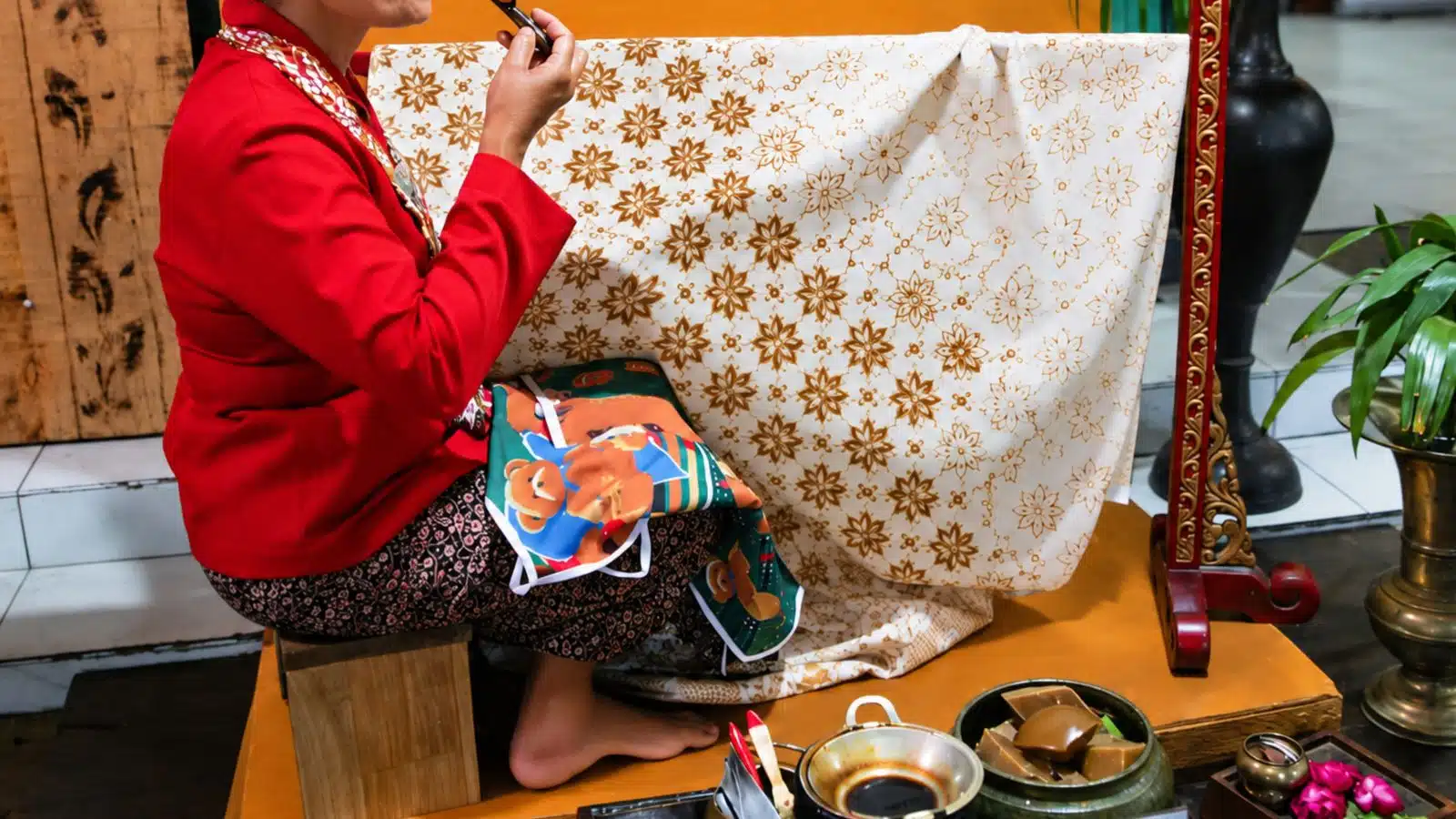Perajin batik tulis menorehkan malam dengan canting di depan kain bermotif bunga kecil